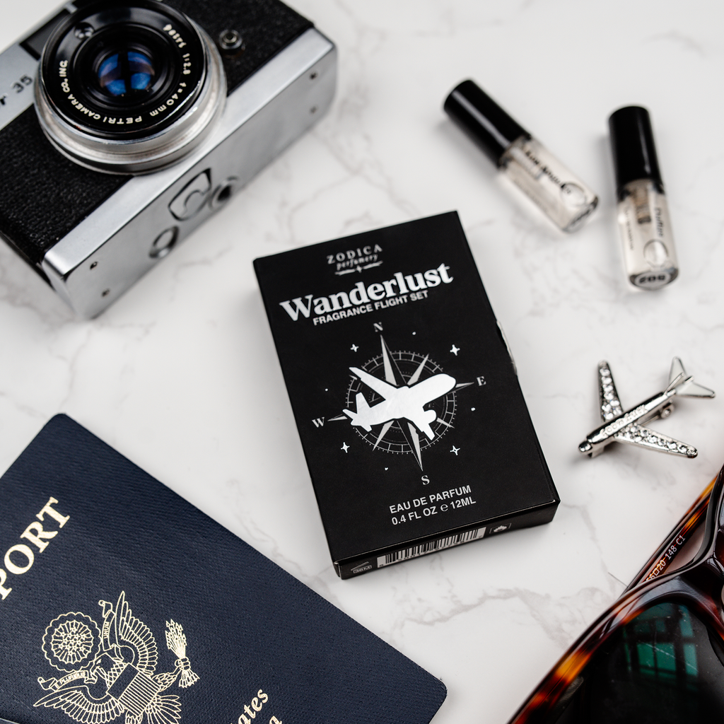 Zodica Wanderlust perfume set with camera, passport, sunglasses, and airplane model on a white surface