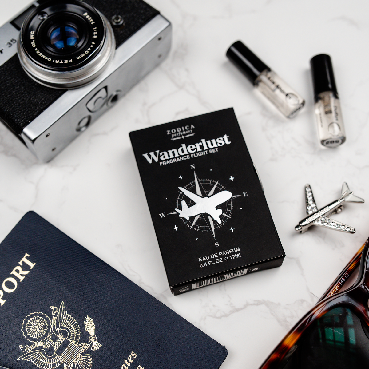 Zodica Wanderlust perfume set with camera, passport, sunglasses, and airplane model on a white surface