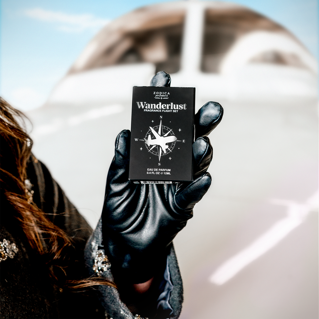 Kristi Moe holding a black Wanderlust fragrance set packaging against a blurred jet background