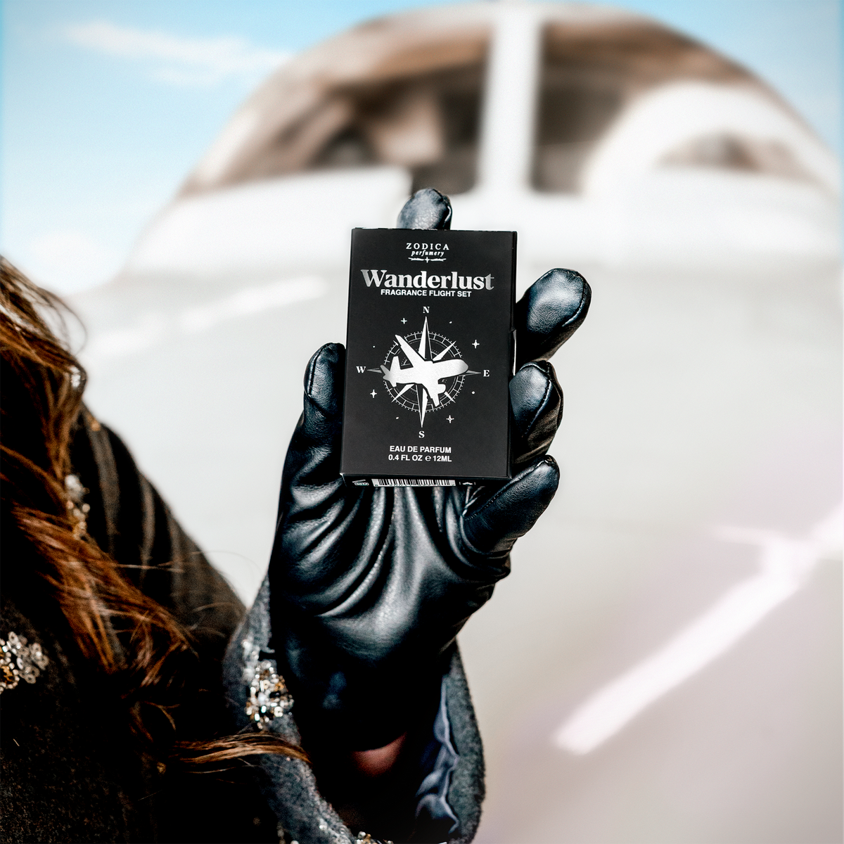 Kristi Moe holding a black Wanderlust fragrance set packaging against a blurred jet background