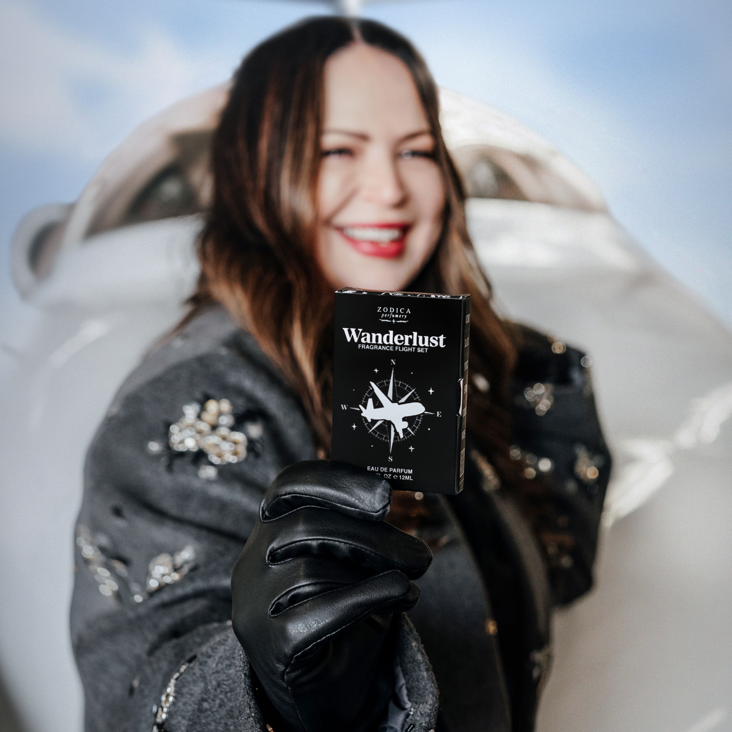 Kristi Moe holding a 'Wanderlust' perfume passport product box with a scenic background
